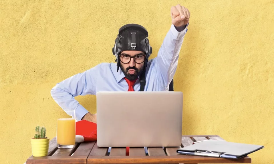 Man in helmet making victory gesture at laptop.