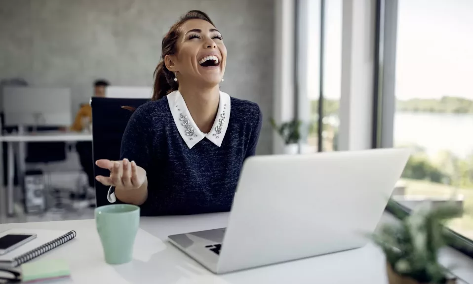 Joyful woman laughing at desk with laptop